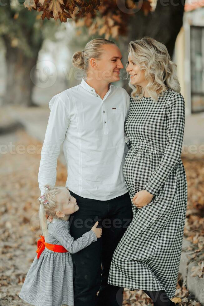 portrait de une Jeune Enceinte femme avec sa famille à l'extérieur dans une parc parmi jauni feuilles photo