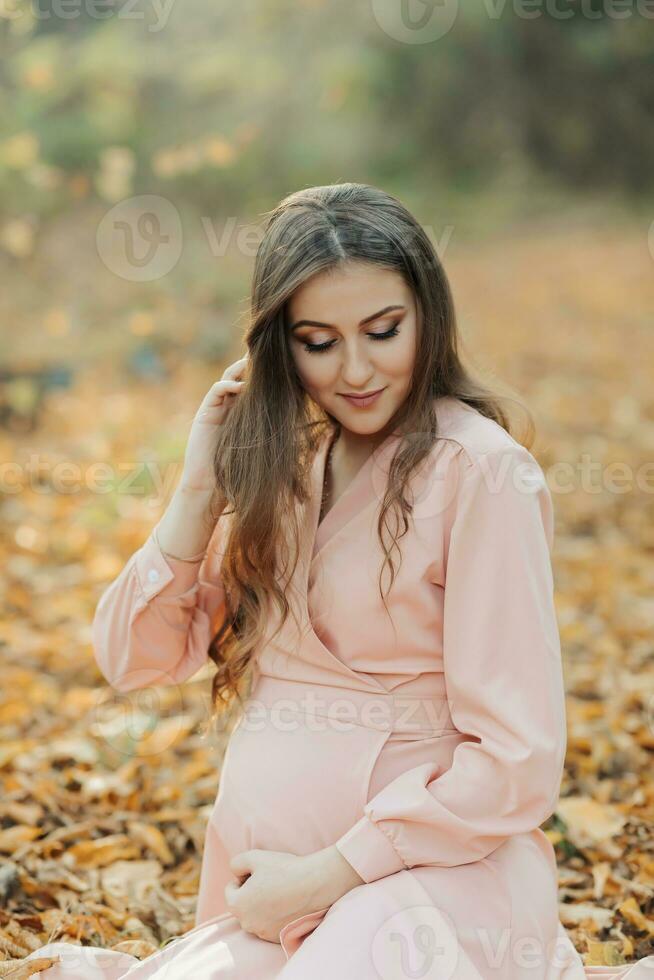 portrait de une Jeune Enceinte femme séance sur une jauni l'automne feuille photo