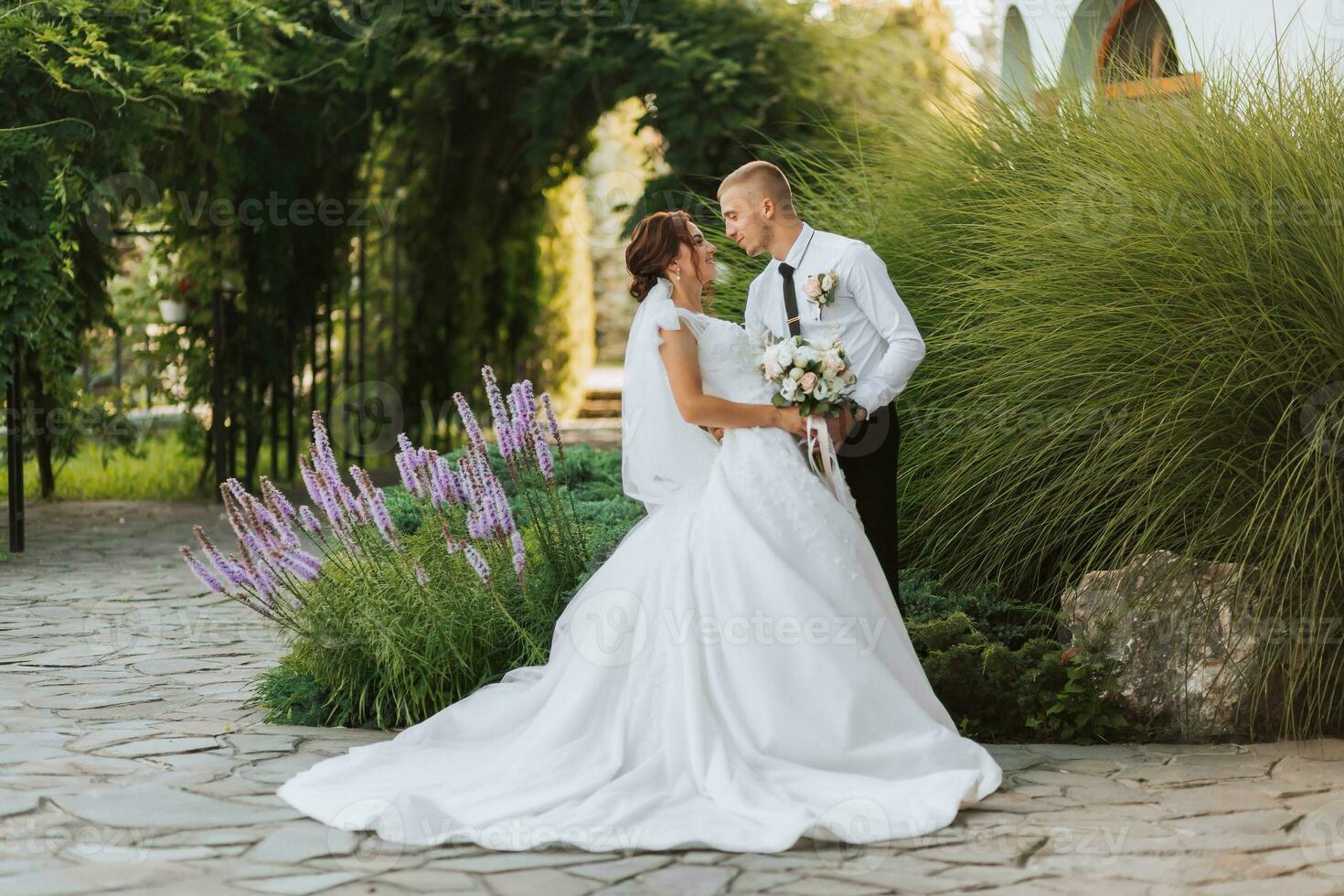 portrait de le la mariée et jeune marié dans le parc, le la mariée et jeune marié sont posant près lavande fleurs. mariage marcher dans le parc. longue train de le robe photo