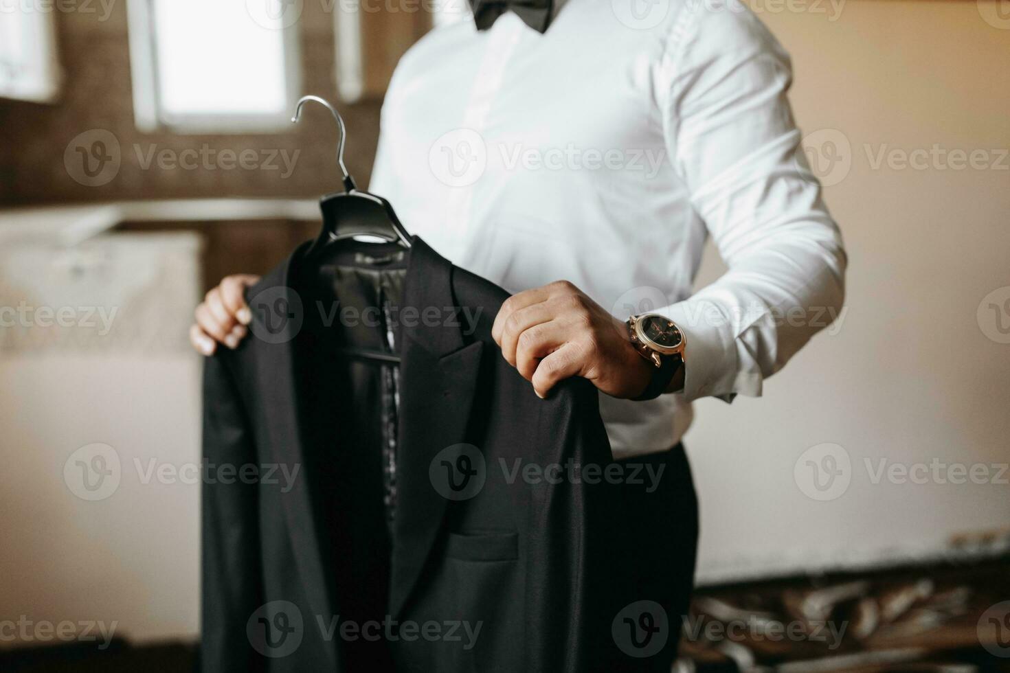 le homme détient le sien noir veste sur une cintre dans le sien mains. le jeune marié est en train de préparer pour le mariage cérémonie. détaillé fermer photo de mains
