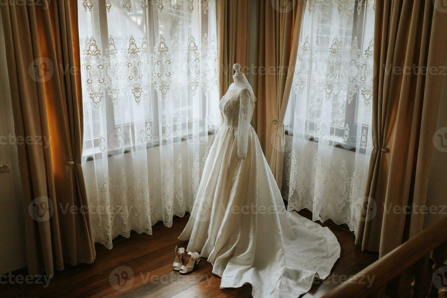 une luxueux dentelle mariage robe dans un coûteux intérieur de une Hôtel illuminé par Naturel lumière de une fenêtre sur deux côtés photo