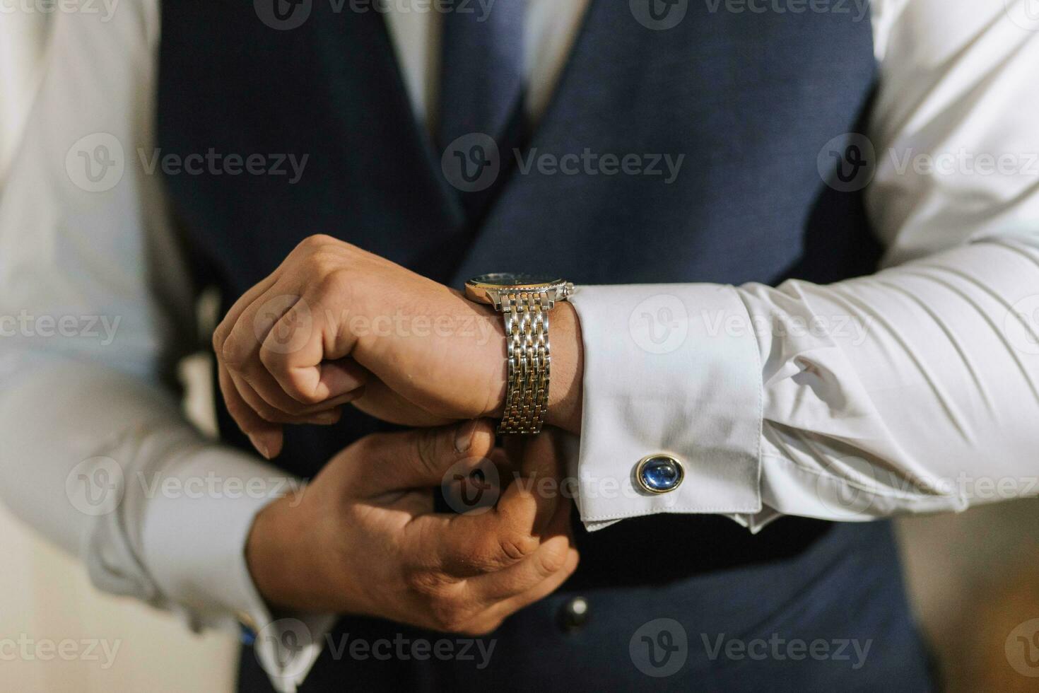 une homme regarder dans le sien mains. une homme ajuste et met sur une regarder sur le sien poignet. le jeune marié est en train de préparer pour le mariage photo