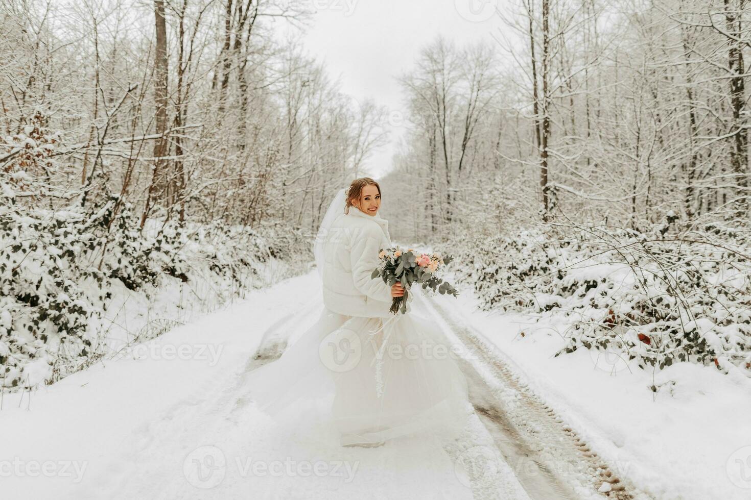 une magnifique la mariée dans blanc est en marchant vers le bas le route dans une fabuleux neigeux hiver forêt. portrait de le la mariée dans la nature. magnifique la mariée dans une blanc robe dans une hiver forêt. photo