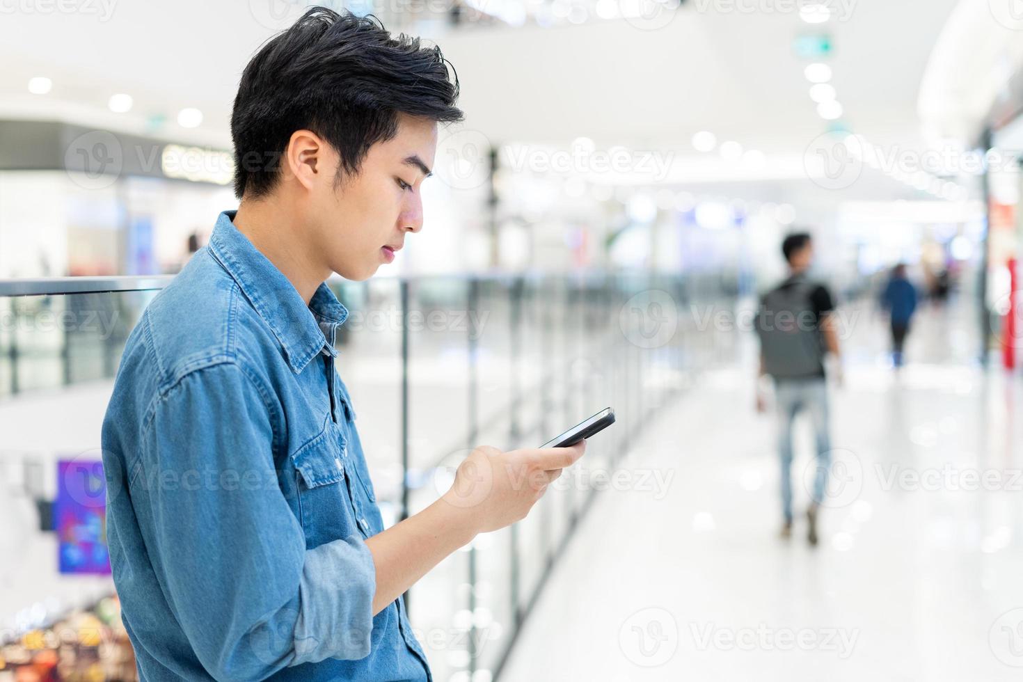 mains d'un jeune homme asiatique, utilisant un téléphone mobile intelligent, sur fond flou de centre commercial. photo