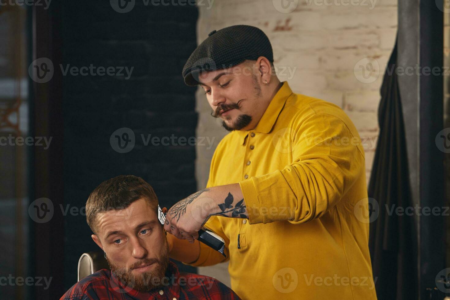 Barbier faisant la coupe de cheveux d'un homme barbu attrayant en salon de coiffure photo