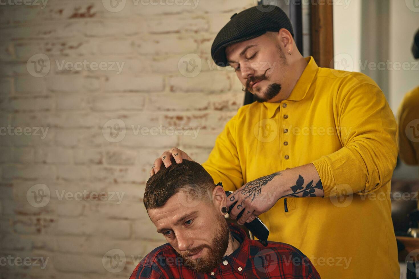 Barbier faisant la coupe de cheveux d'un homme barbu attrayant en salon de coiffure photo