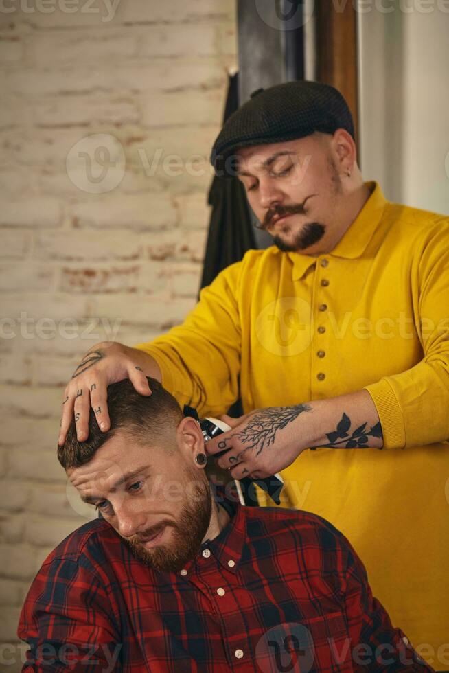 Barbier faisant la coupe de cheveux d'un homme barbu attrayant en salon de coiffure photo