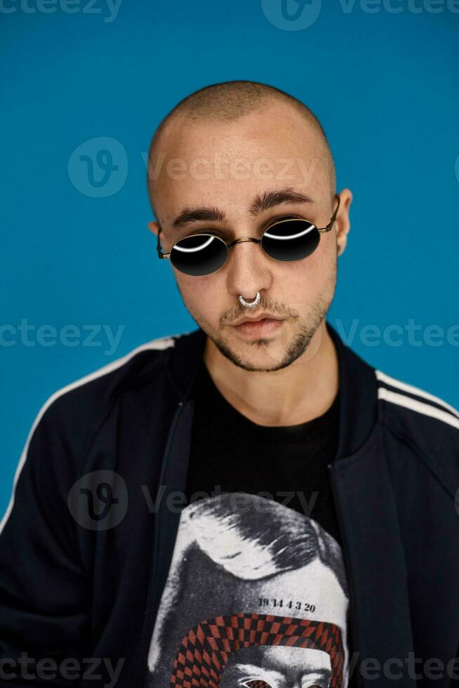 studio coup de une Jeune tatoué chauve homme posant contre une bleu Contexte. Années 90 style. photo