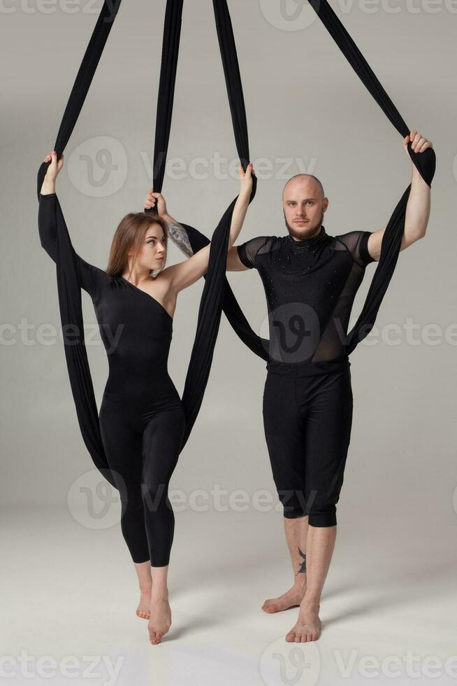 magnifique fille et un athlétique homme dans une noir sport costume sont performant un acrobatique éléments dans une studio. photo