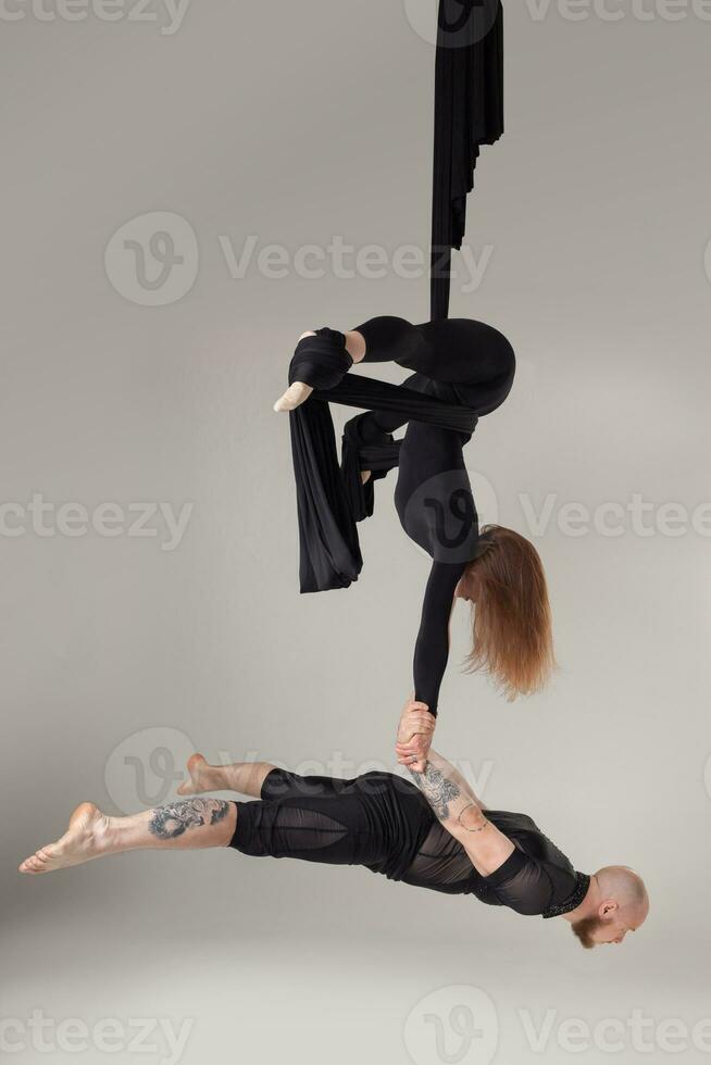 magnifique fille et un athlétique homme dans une noir sport costume sont performant un acrobatique éléments dans une studio. photo