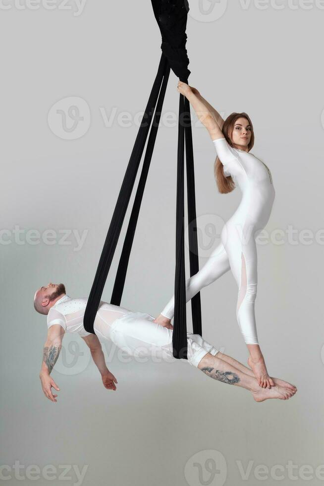 magnifique fille et un athlétique homme dans une blanc sport costume sont performant un acrobatique éléments dans une studio. photo