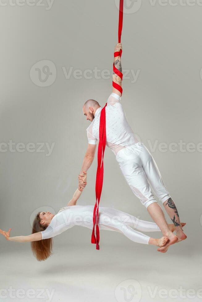 magnifique fille et un athlétique homme dans une blanc sport costume sont performant un acrobatique éléments dans une studio. photo