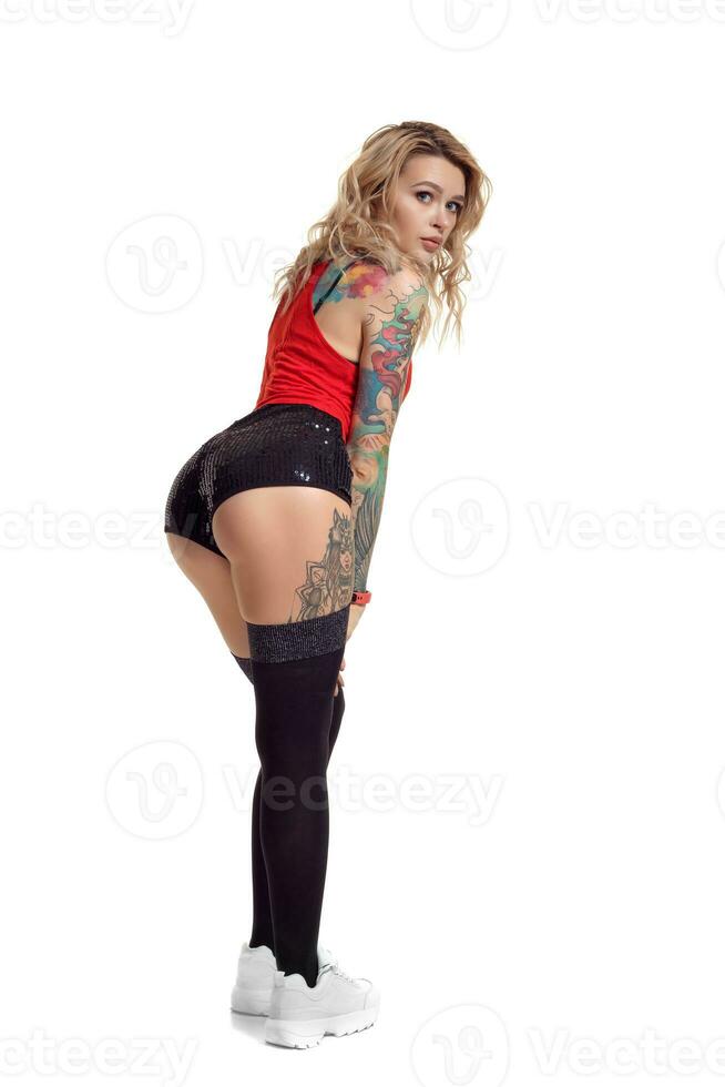 sexy blond twerk femme avec tatoué corps et longue frisé cheveux est posant dans studio. photo