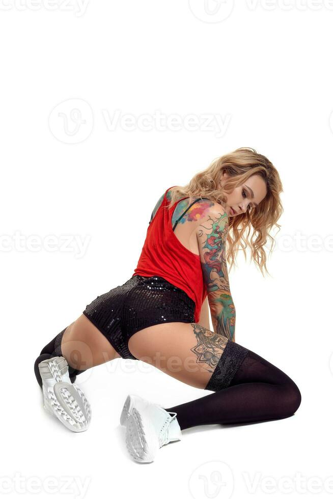 sexy blond twerk femme avec tatoué corps et longue frisé cheveux est posant dans studio. photo