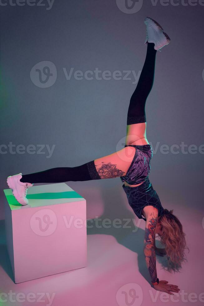 Jeune magnifique blond gymnaste fille dans velours bleu butin short et noir bas permanent à l'envers vers le bas sur rose Contexte photo