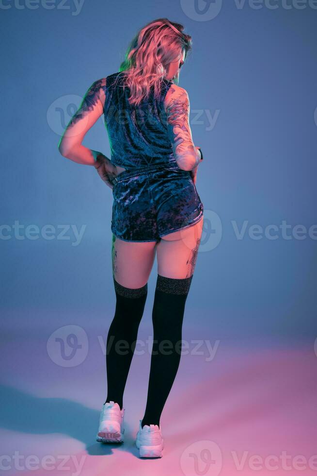 Jeune blond femme dans velours bleu sport porter et noir bas de façon séduisante posant sur caméra dans studio. rose et bleu Contexte photo