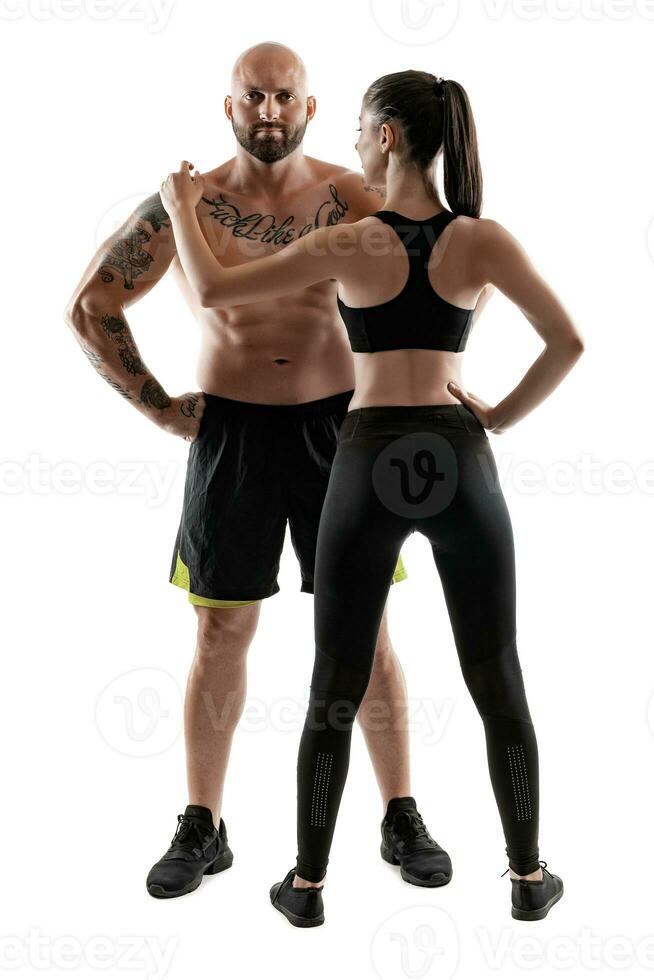 athlétique homme dans noir short et baskets avec brunette femme dans leggings et Haut posant isolé sur blanc Contexte. aptitude couple, Gym concept. photo