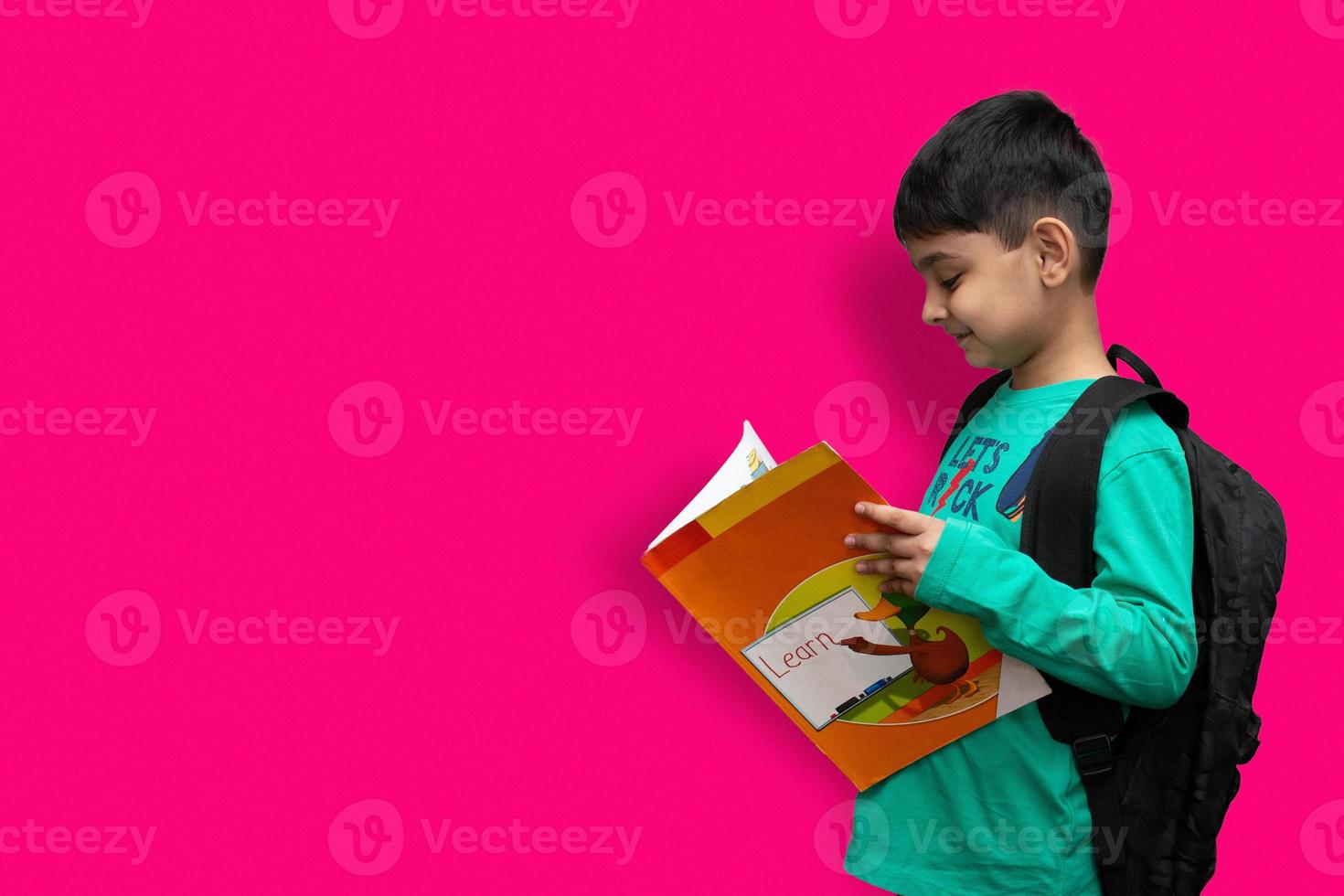 mignon garçon heureux de 7 ans avec sac à dos scolaire tenant des livres en arrière-plan uni pour le concept d'éducation photo