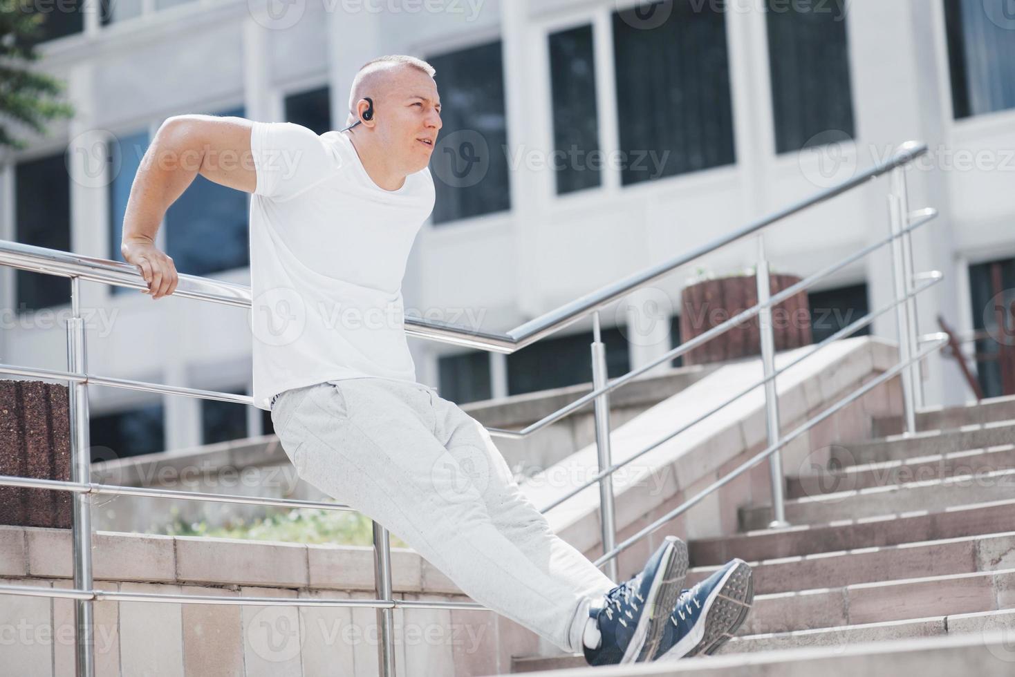 un bel homme de remise en forme dans un vêtement de sport, faisant des étirements tout en se préparant à un exercice sérieux dans la ville moderne photo