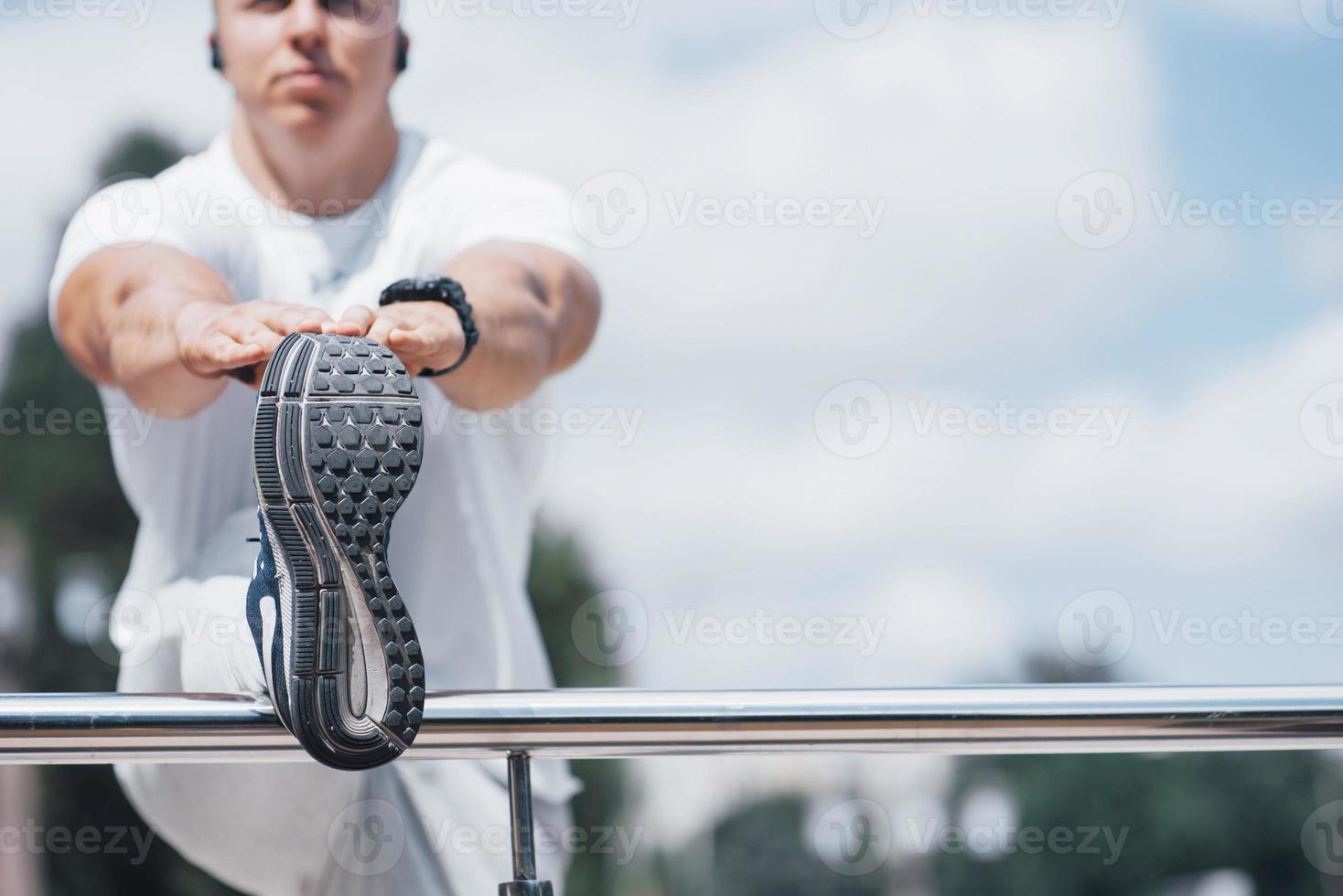 un bel homme de remise en forme dans un vêtement de sport, faisant des étirements tout en se préparant à un exercice sérieux dans la ville moderne photo