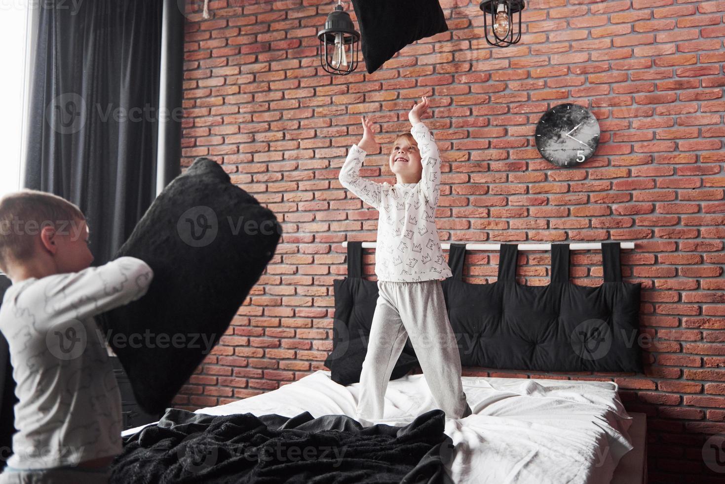 vilains enfants petit garçon et fille ont organisé une bataille d'oreillers sur le lit dans la chambre. ils aiment ce genre de jeu photo