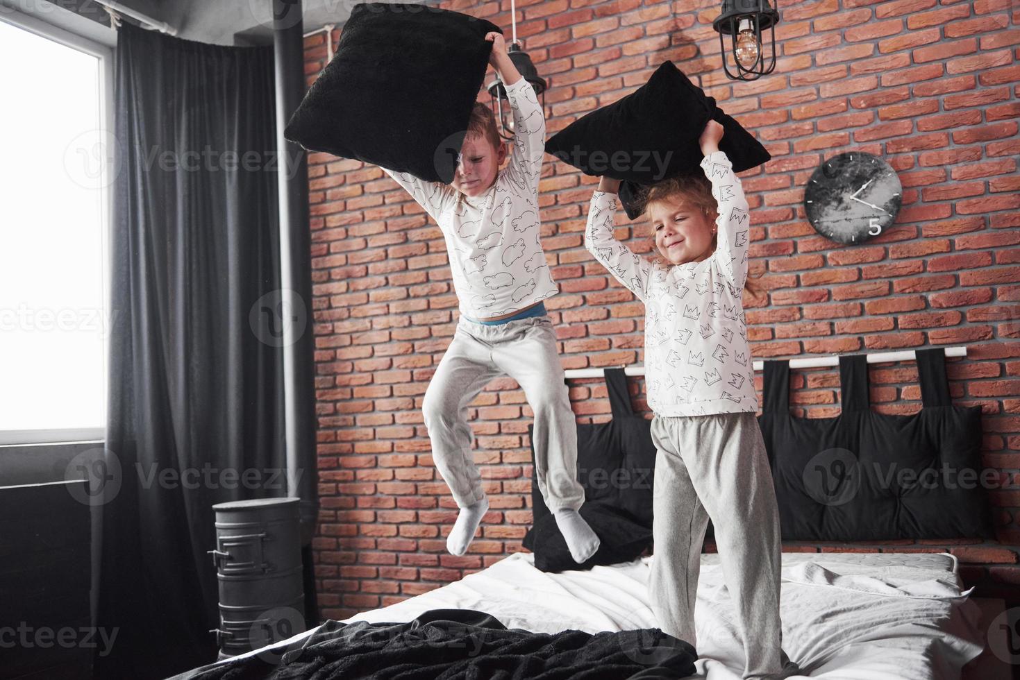 vilains enfants petit garçon et fille ont organisé une bataille d'oreillers sur le lit dans la chambre. ils aiment ce genre de jeu photo