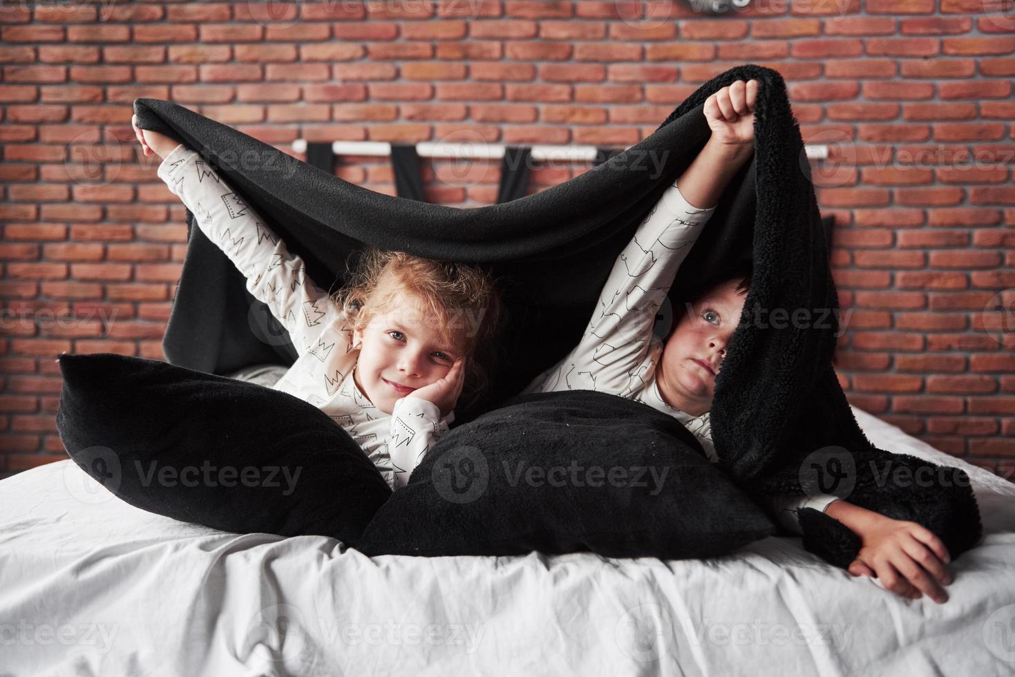 petits enfants, garçon et fille allongés et jouant avec des oreillers sur le couvre-lit avec une couverture photo
