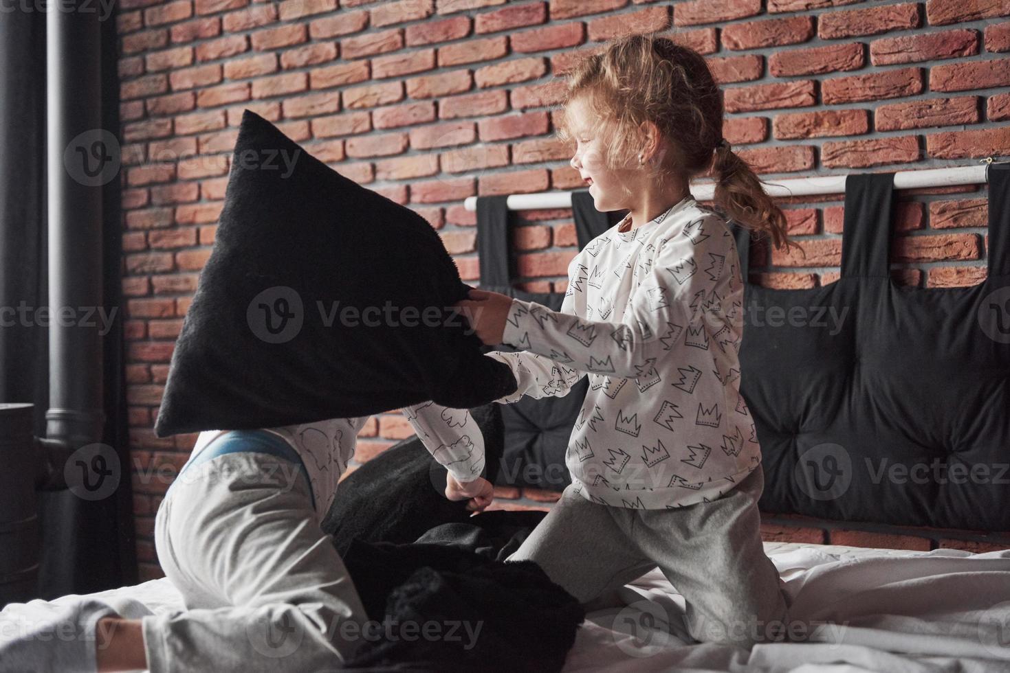 vilains enfants petit garçon et fille ont organisé une bataille d'oreillers sur le lit dans la chambre. ils aiment ce genre de jeu photo