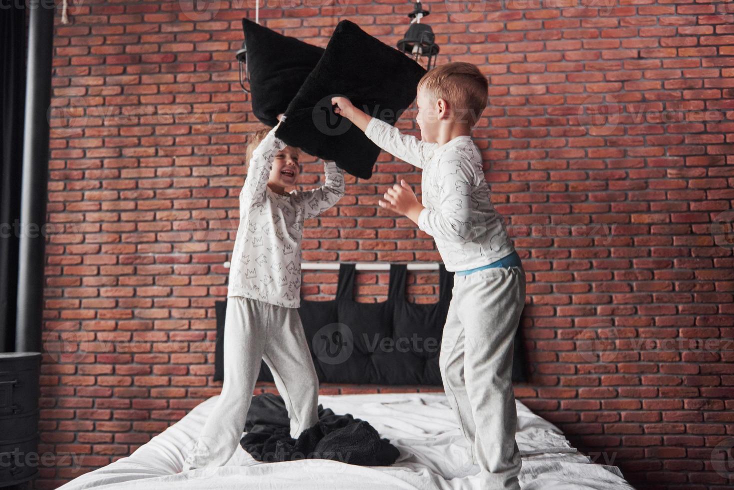 vilains enfants petit garçon et fille ont organisé une bataille d'oreillers sur le lit dans la chambre. ils aiment ce genre de jeu photo