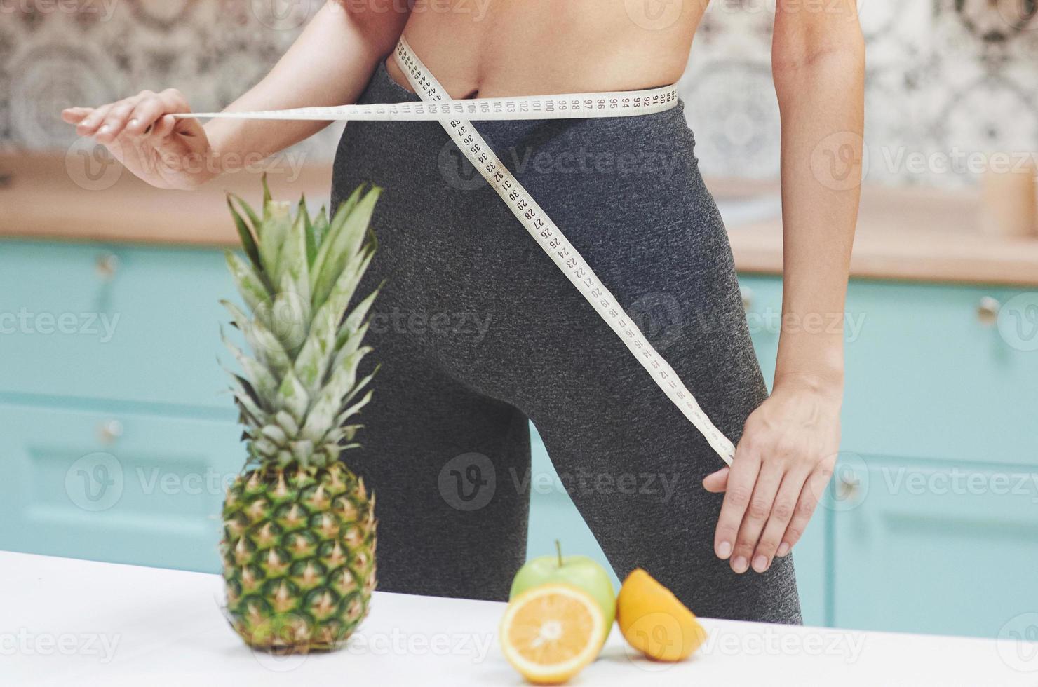 portrait d'une femme mesurant son corps mince sur un fond de cuisine. concept de remise en forme et de mode de vie sain photo