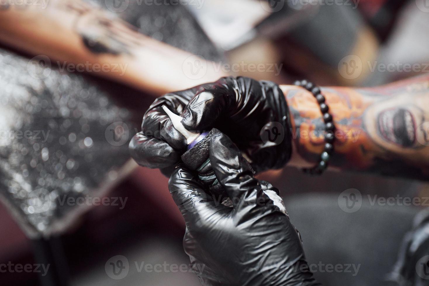 fermer la machine à tatouer. maître en gants stériles noirs créant une image à portée de main avec lui dans le salon photo