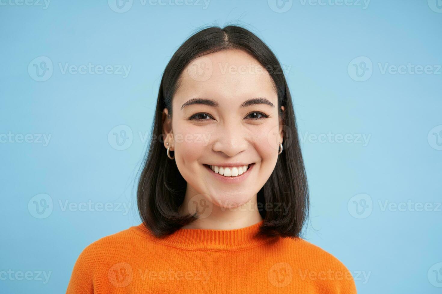 proche en haut portrait de magnifique coréen femme avec en bonne santé sourire, Naturel clair faciale peau, des stands plus de bleu Contexte photo