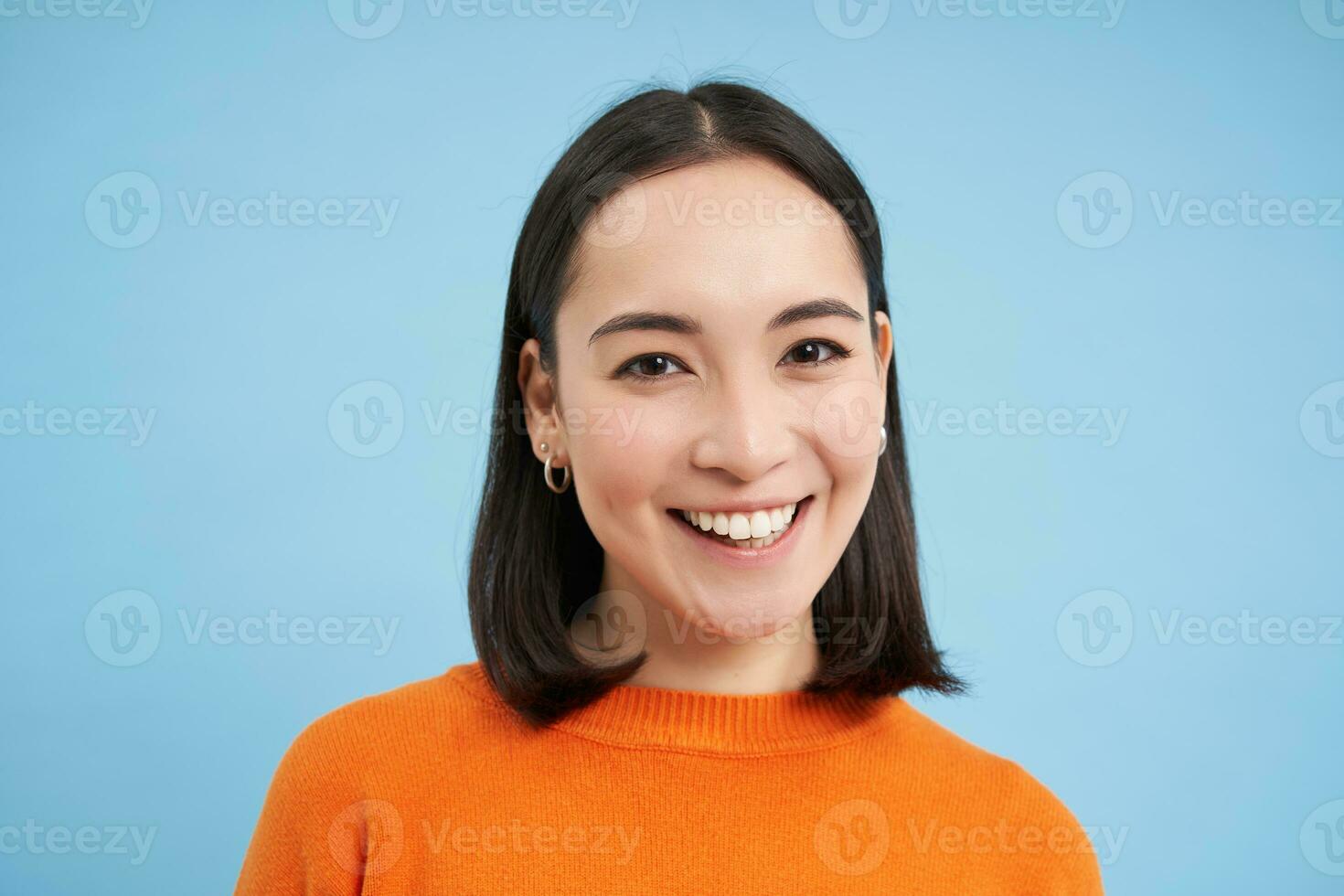 proche en haut portrait de magnifique coréen femme avec en bonne santé sourire, Naturel clair faciale peau, des stands plus de bleu Contexte photo