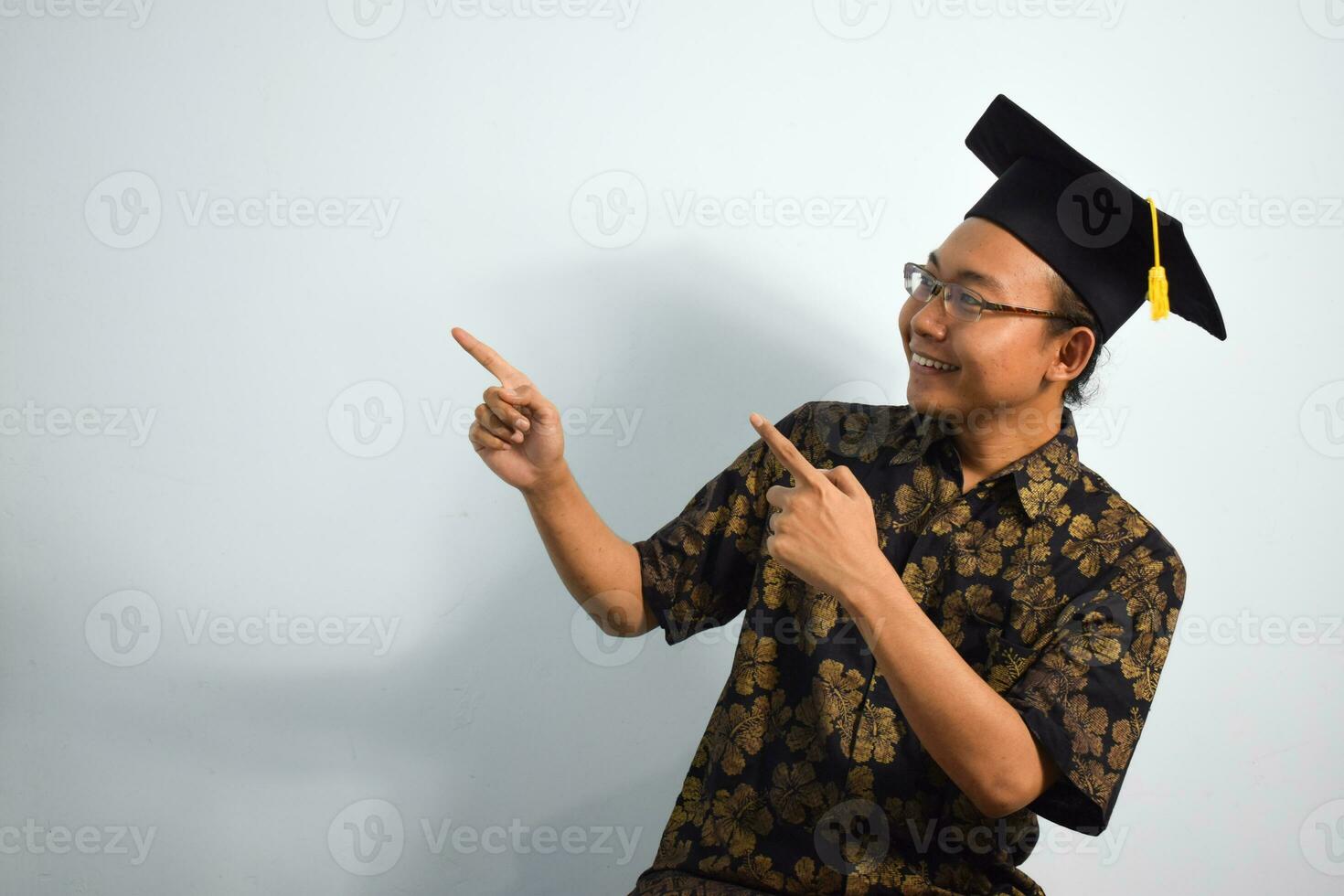 expressif de adulte Indonésie Masculin porter batique, toge tasse ou l'obtention du diplôme chapeau et lunettes isolé sur blanc arrière-plan, expressions de portrait l'obtention du diplôme photo