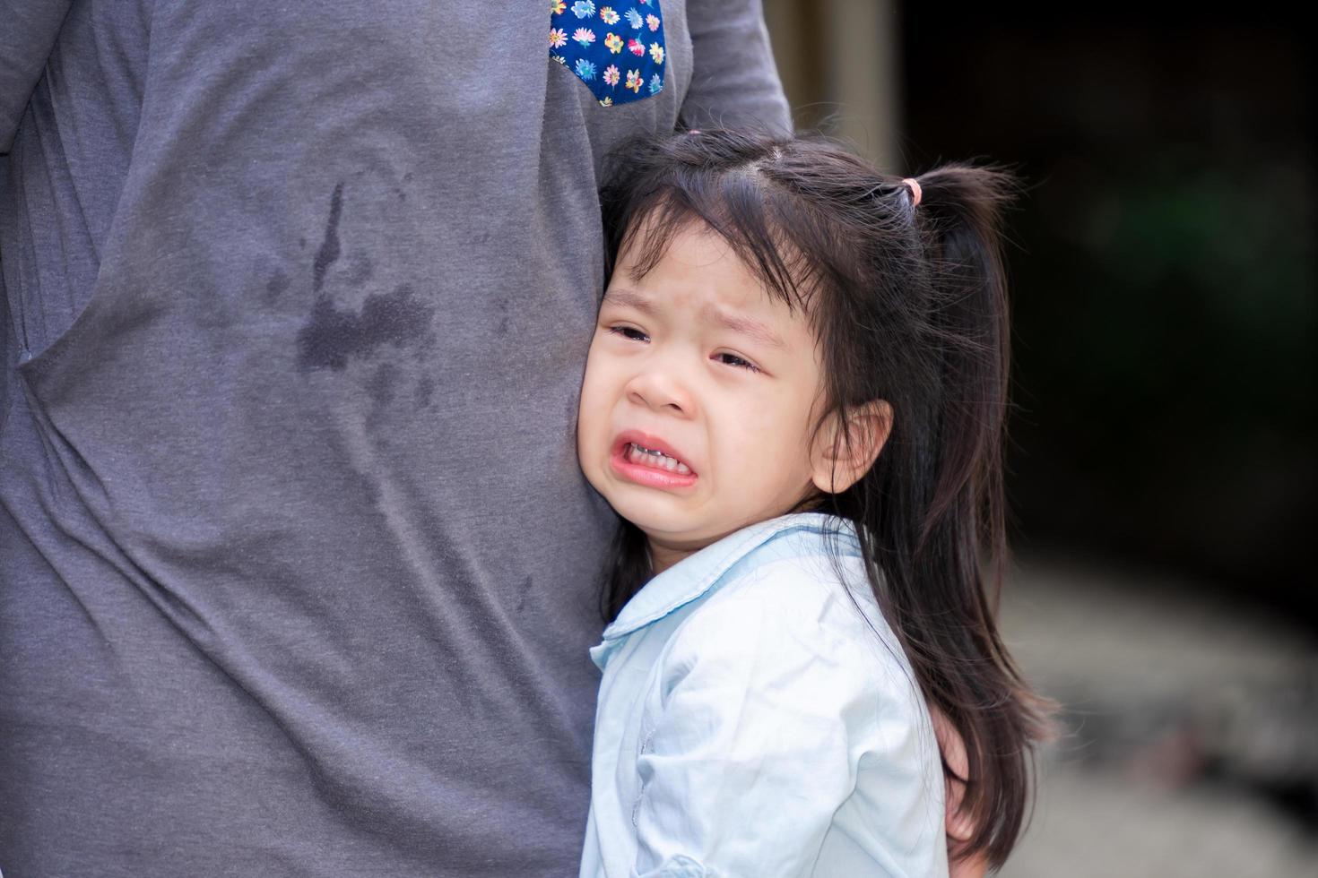 adorable fille asiatique pleure avec des larmes sur les joues. enfant reposait sur le ventre de sa mère. les enfants souffrent de chagrin d'amour. un enfant de 4 ans porte des chemises bleu clair. photo