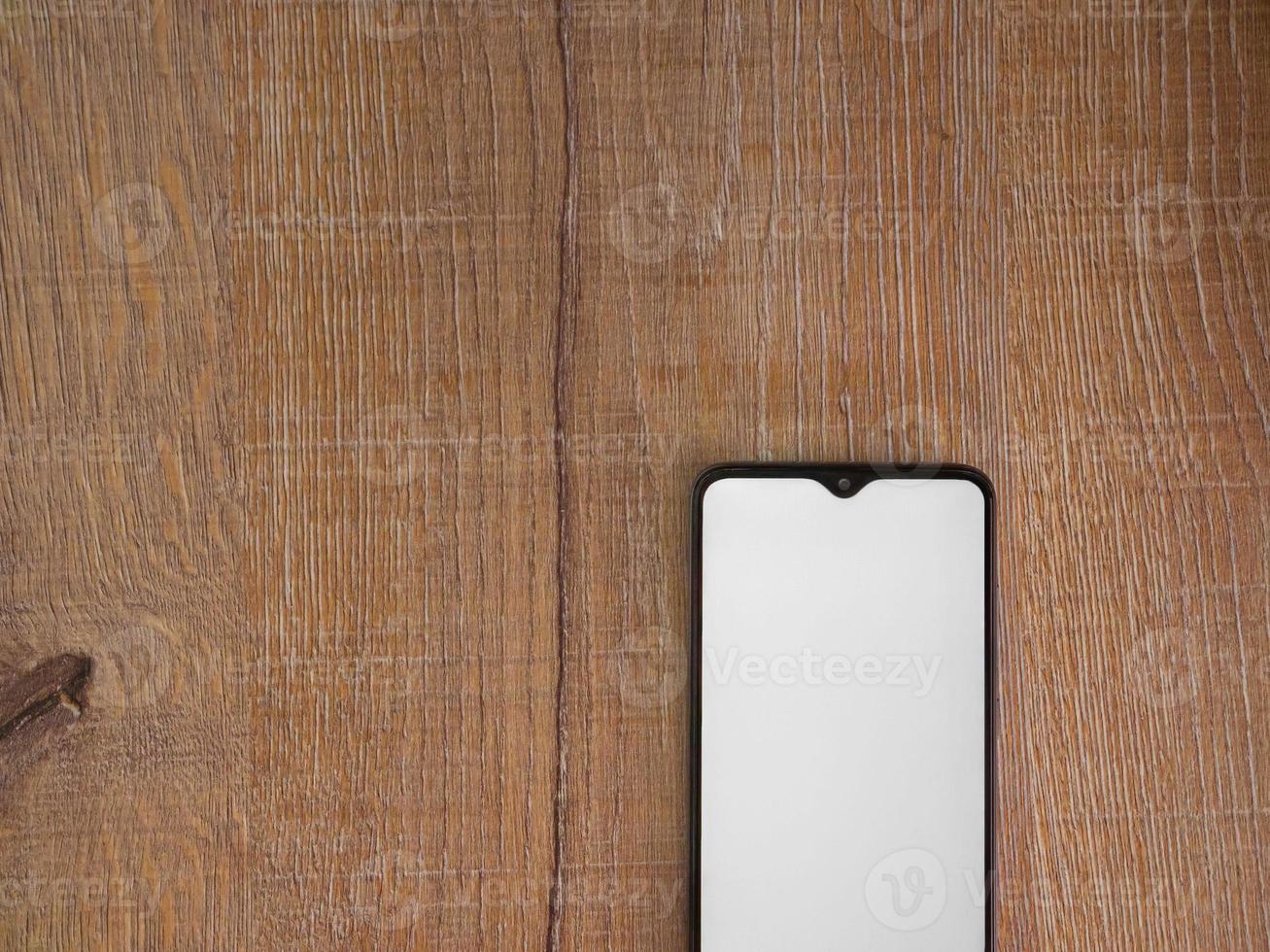 maquette de smartphone mobile noir se trouve à la surface avec écran blanc isolé sur fond de bois photo