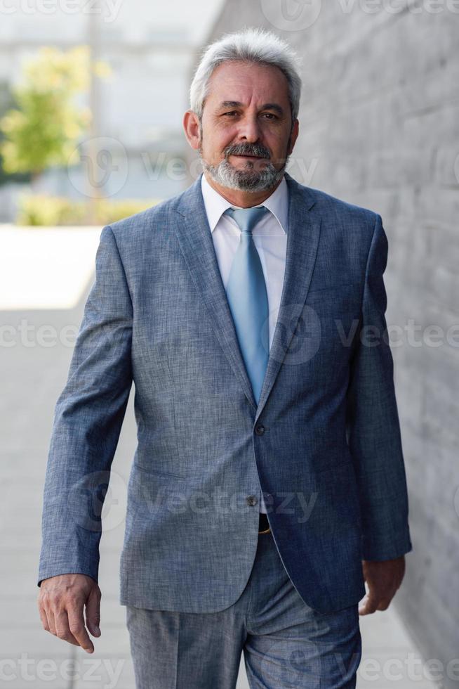 homme d'affaires senior marchant à l'extérieur d'un immeuble de bureaux moderne. photo