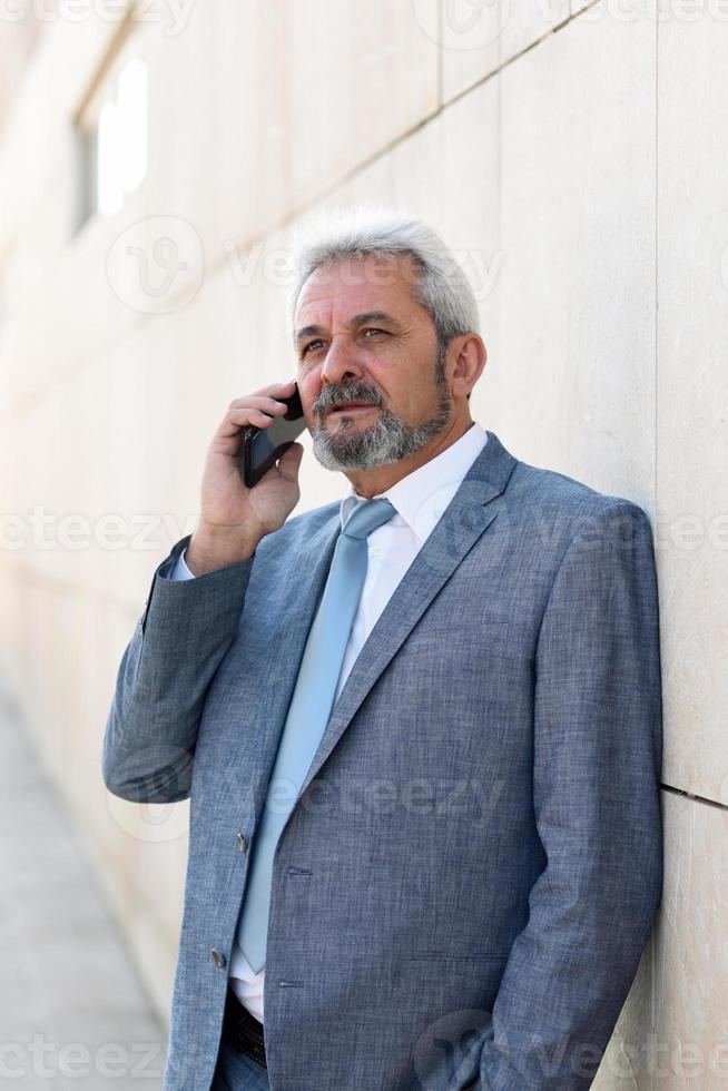 homme d'affaires senior avec smartphone à l'extérieur d'un immeuble de bureaux moderne. photo