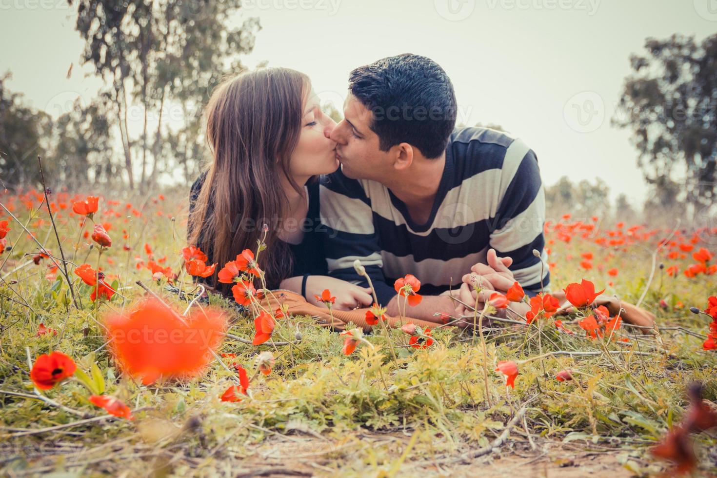 Jeune couple s'embrassant en position couchée sur l'herbe dans un champ de coquelicots rouges photo