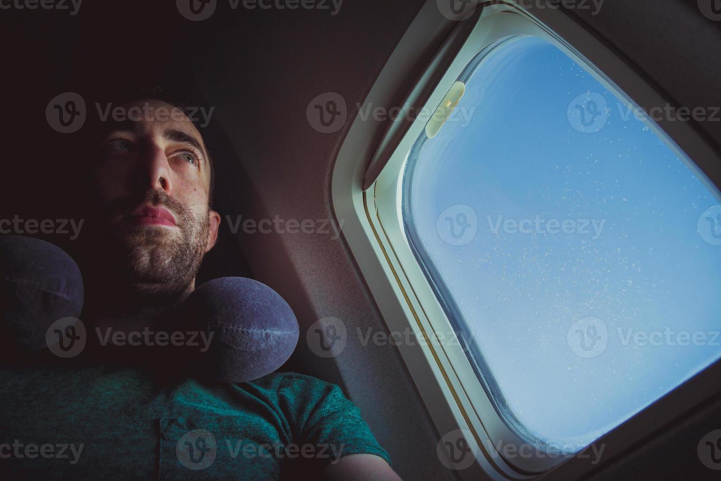 homme pensif avec siège oreiller cervical par la fenêtre d'un avion photo