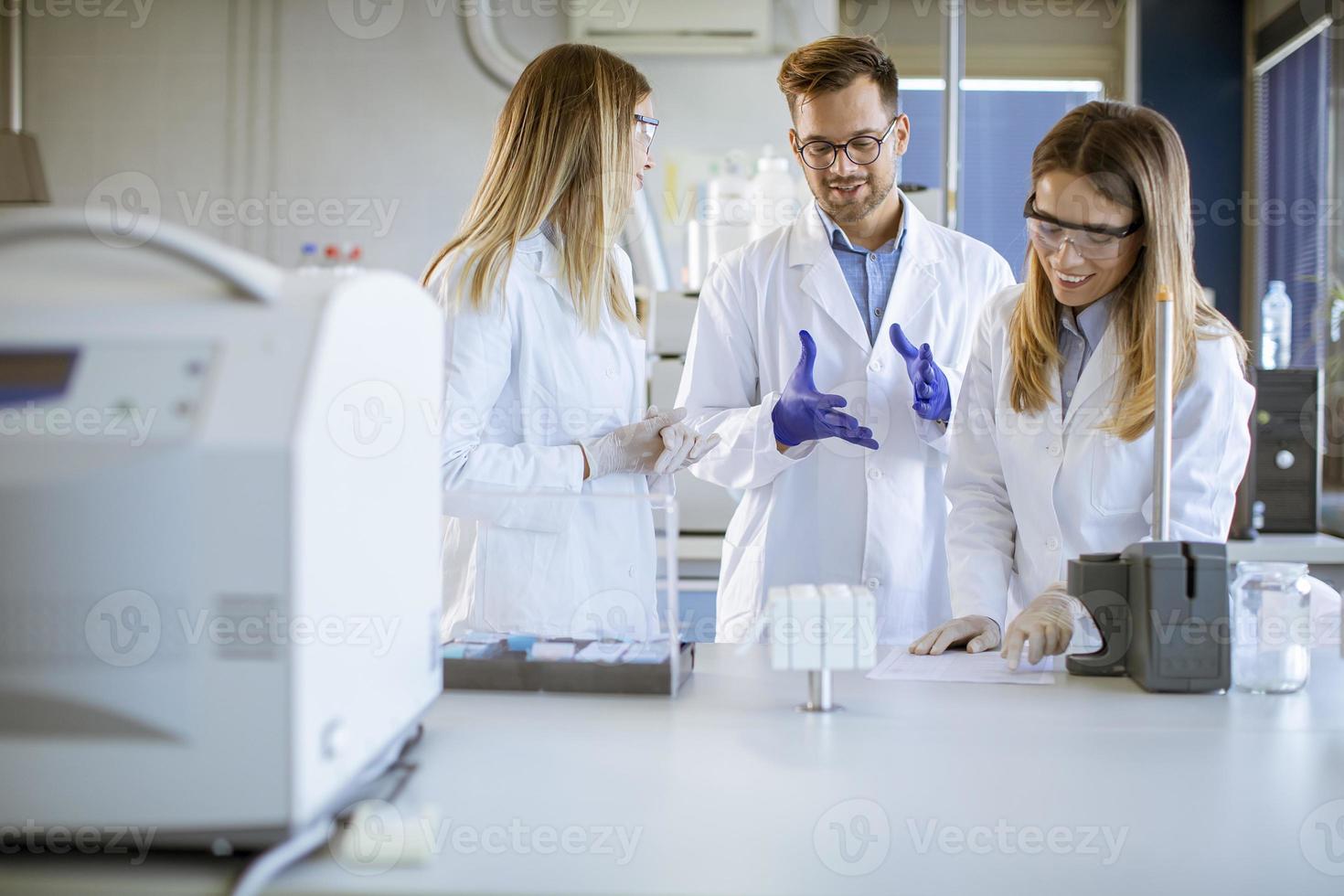 chercheurs en vêtements de travail protecteurs debout dans le laboratoire et analysant des échantillons liquides sur un équipement de chromatographie ionique photo