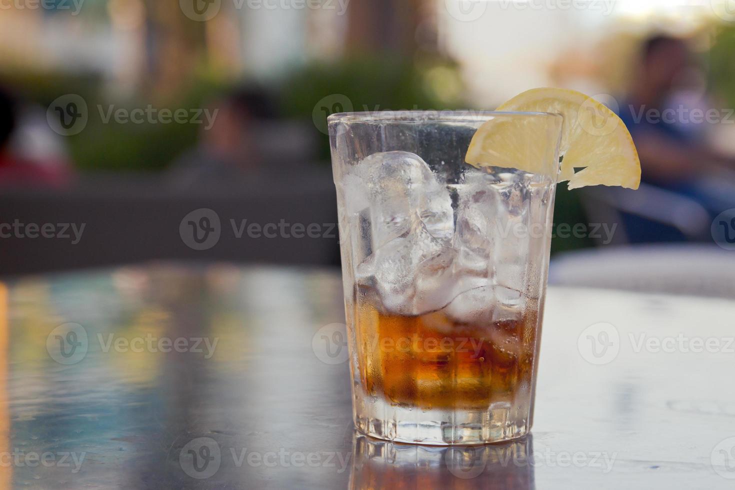 verre avec du cola, de la glace et du citron sur une table à l'extérieur photo