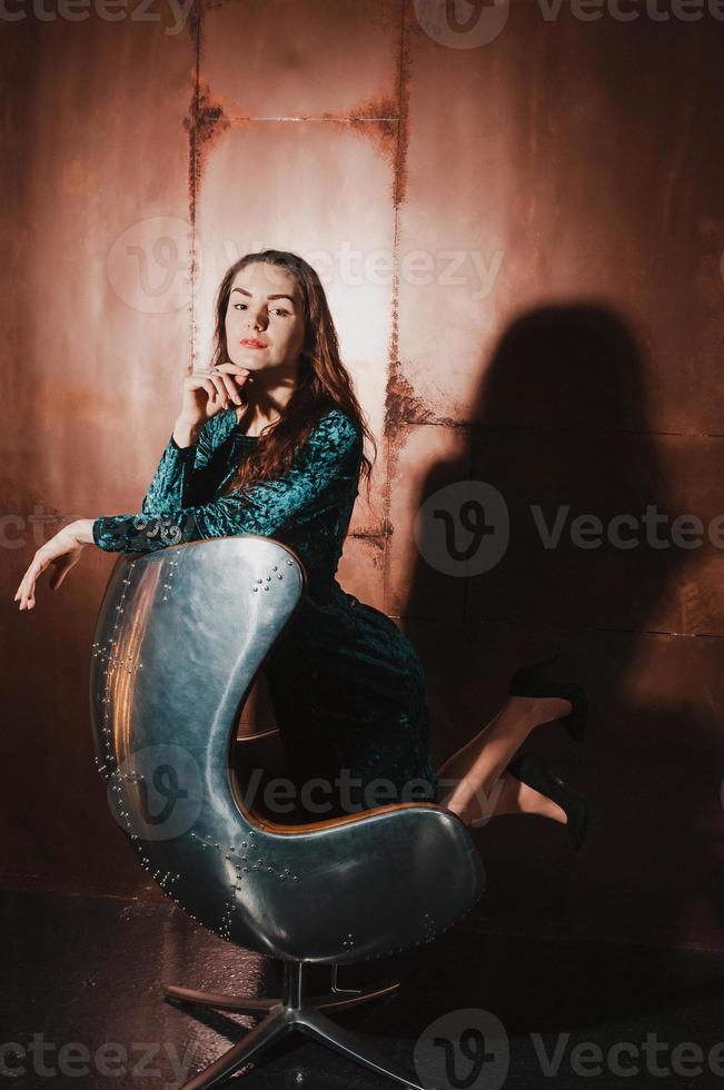 jolie fille en robe de velours, assise dans un fauteuil en cuir marron photo