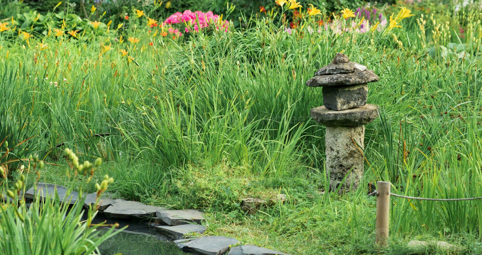 pierre lanterne parmi herbe sur le banque de une étang dans une Japonais jardin photo