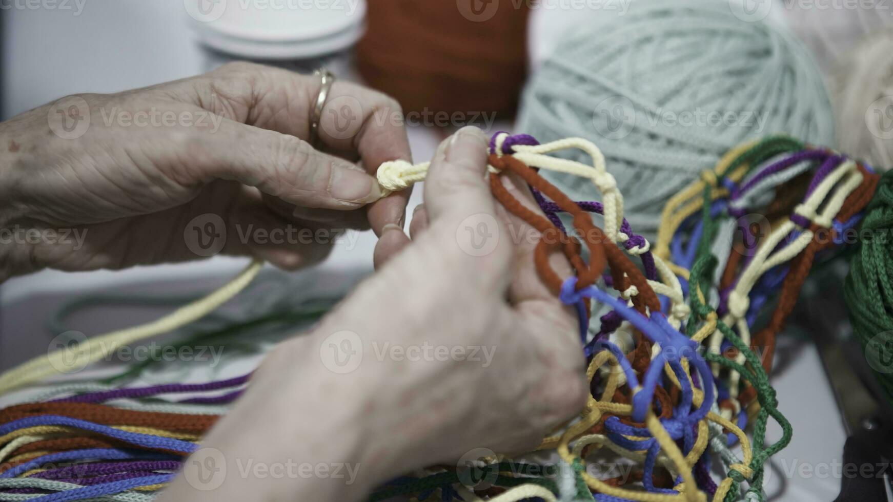 fermer de femme tissage net de Cordes. art. vieux aux femmes mains magistralement attacher noeuds et tisser coloré Cordes dans filet. Créatif juste avec Fait main articles et décorations photo