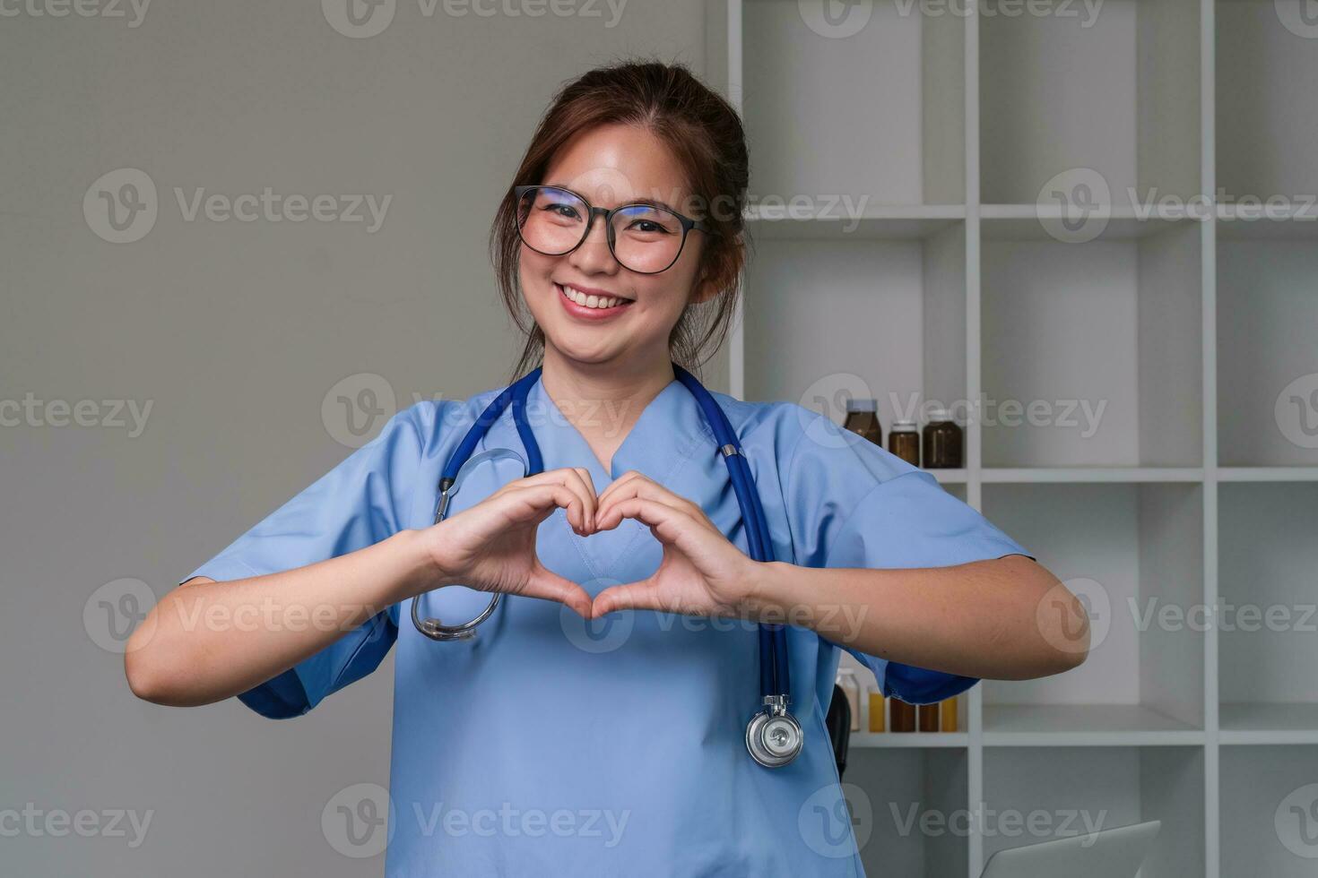 magnifique asiatique femme portant médecin uniforme et stéthoscope souriant dans l'amour Faire cœur symbole forme avec mains. romantique concept. photo
