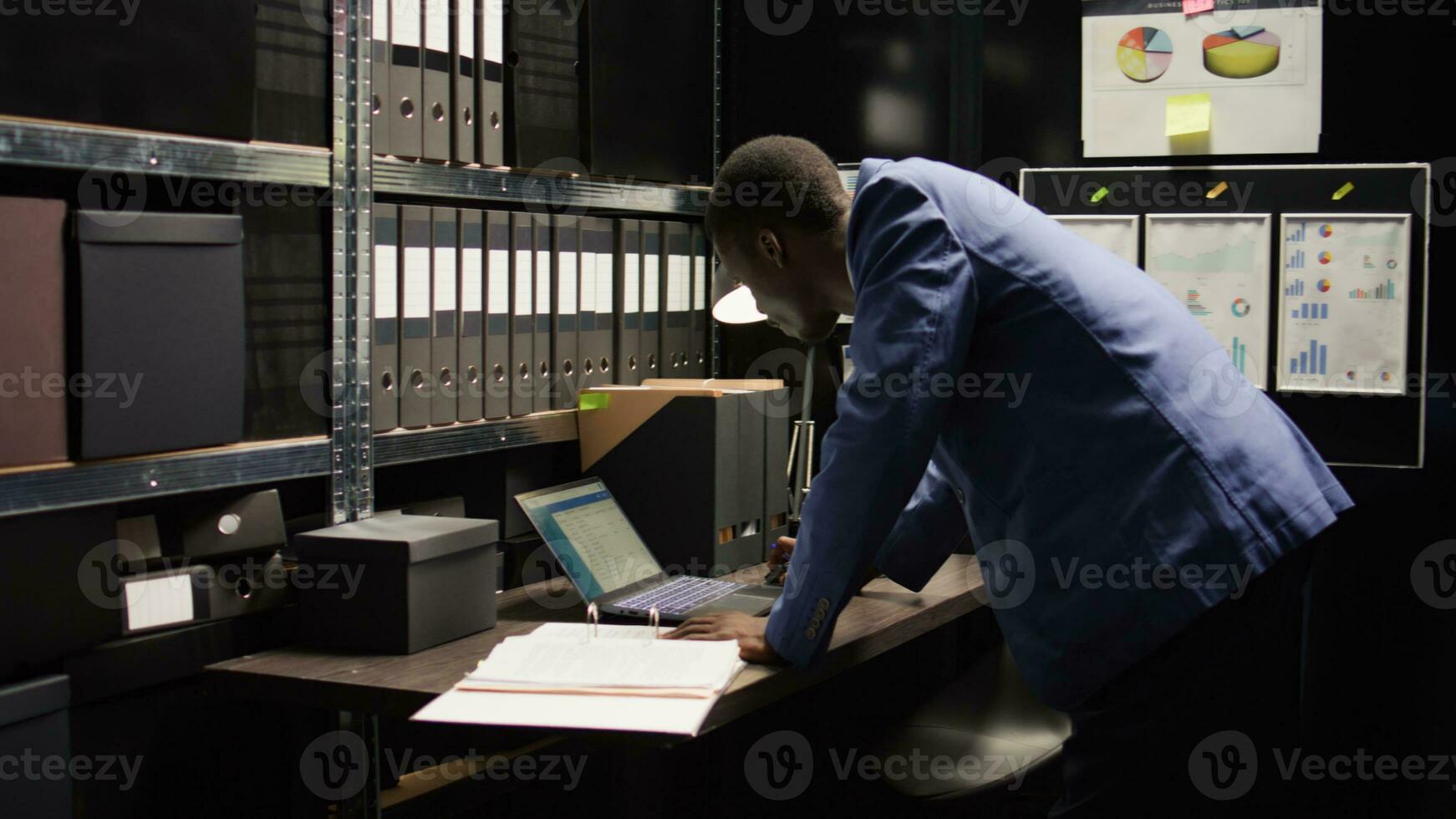 dans soigneusement organisé bureau, africain américain détective examine preuve avec intention de résolution crimes. engagé police officier des promenades en haut à le sien bureau porter Cas fichier pour criminel enquête. photo