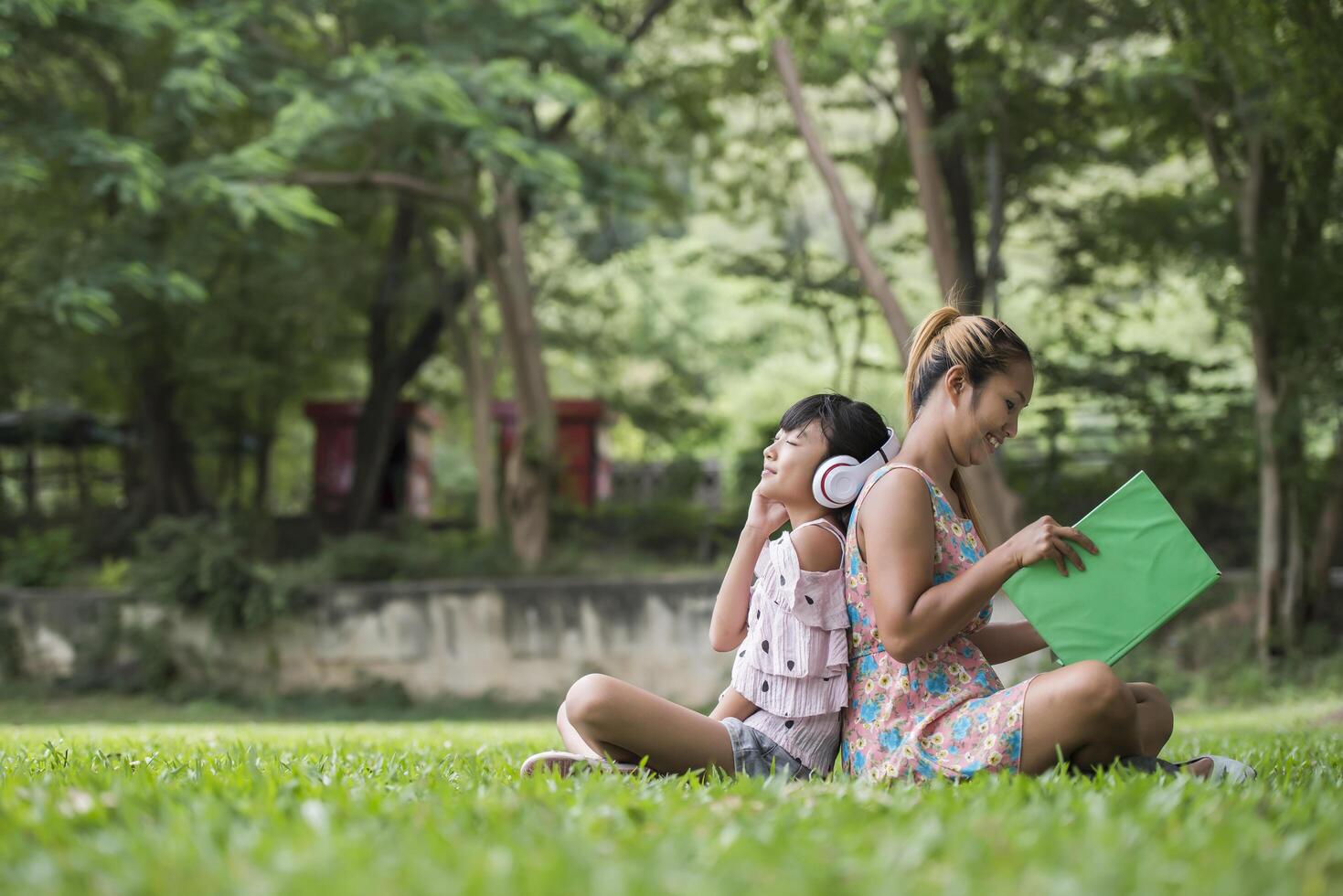 mère et fille lisant un conte de fées à sa fille écoutent le son avec un casque dans le parc photo