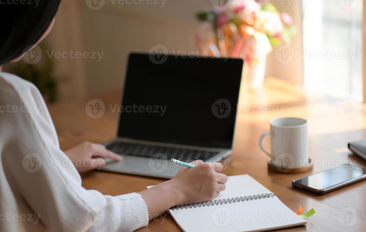 une jeune femme utilise un ordinateur portable et rédige un rapport. elle travaille à domicile. photo