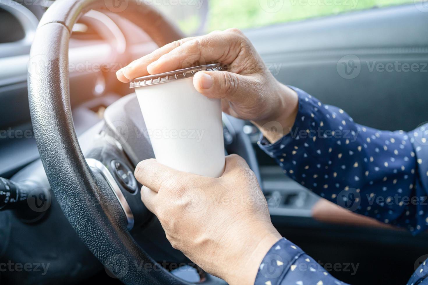 dame asiatique tenant une tasse de café à boire dans la voiture, dangereuse et risquant un accident. photo